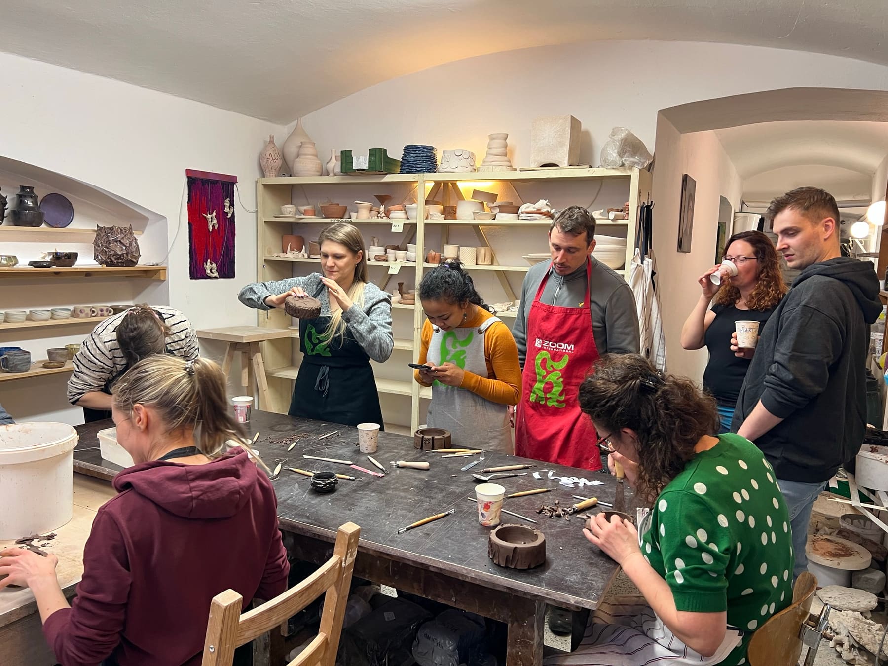 A group gathered around a studio table, shaping clay with hand tools